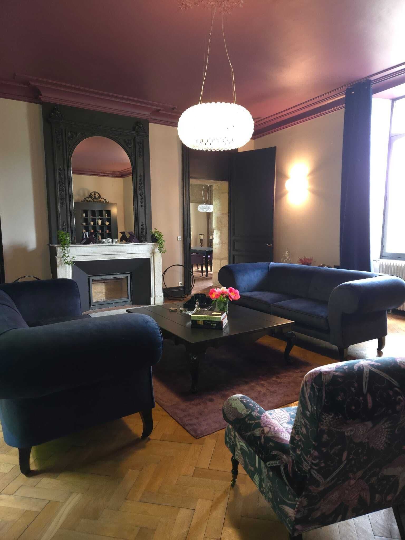 A living room with a fireplace, dark sofas, a coffee table with flowers, and a chandelier.