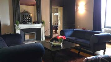 A living room with a fireplace, dark sofas, a coffee table with flowers, and a chandelier.