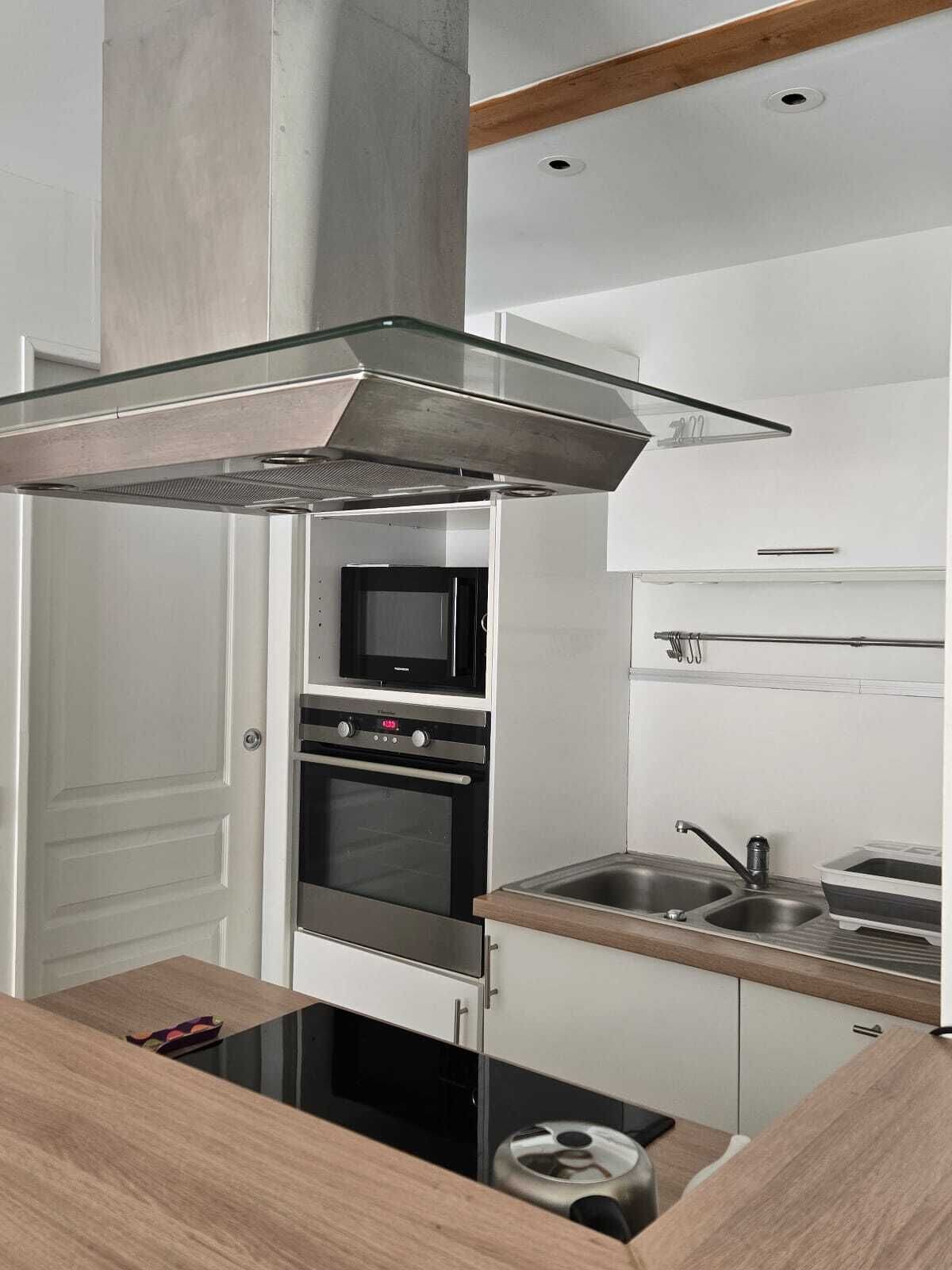 Una cocina moderna con una campana extractora de acero inoxidable, un microondas, un horno y un lavamanos con grifo.