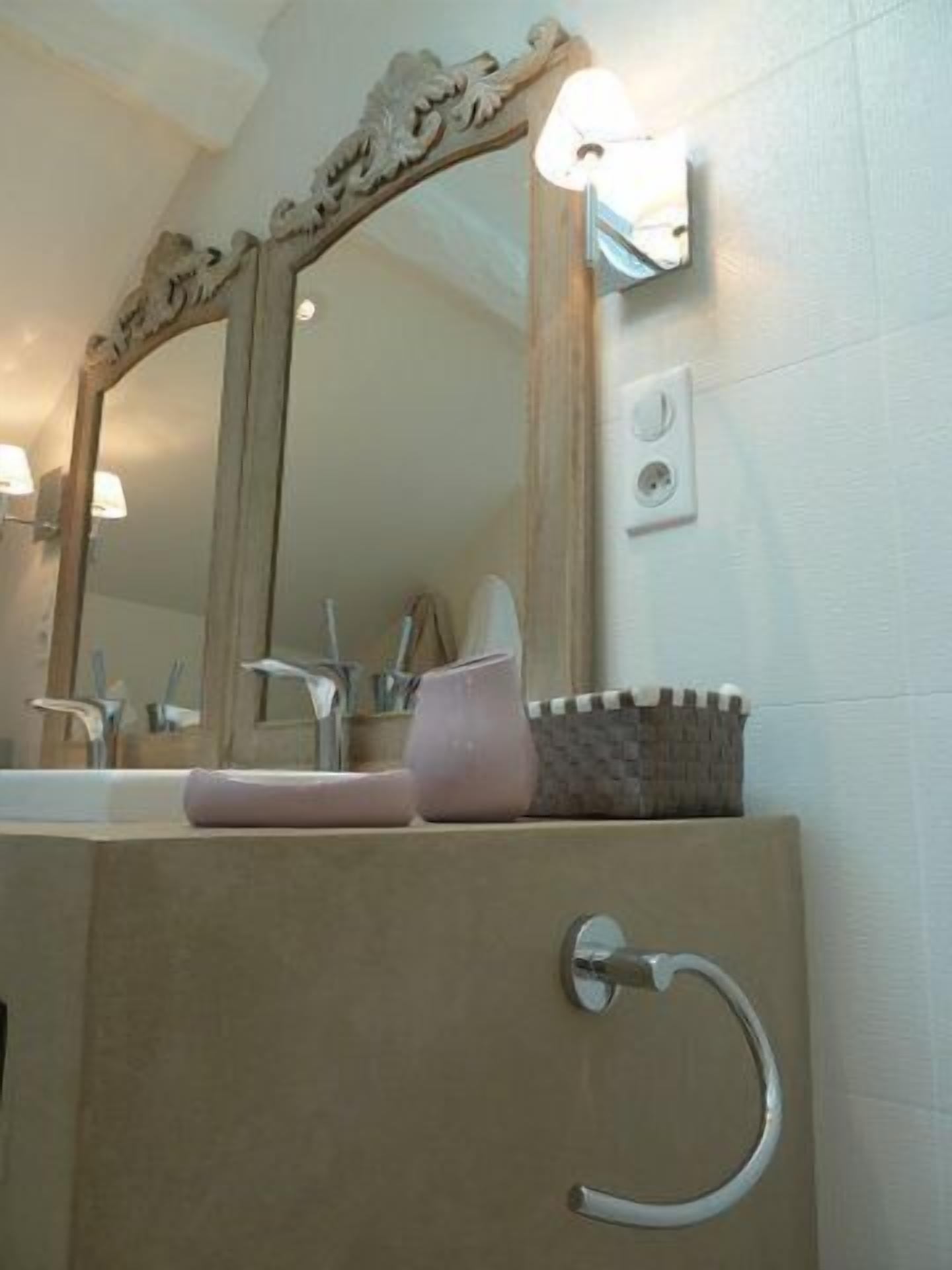 Un baño con un espejo grande, un lavabo con un jabonera rosa y un perchero para toallas.