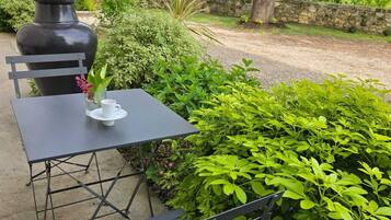 Un espacio al aire libre con mesa y banco, rodeado de abundante vegetación y un muro de piedra.