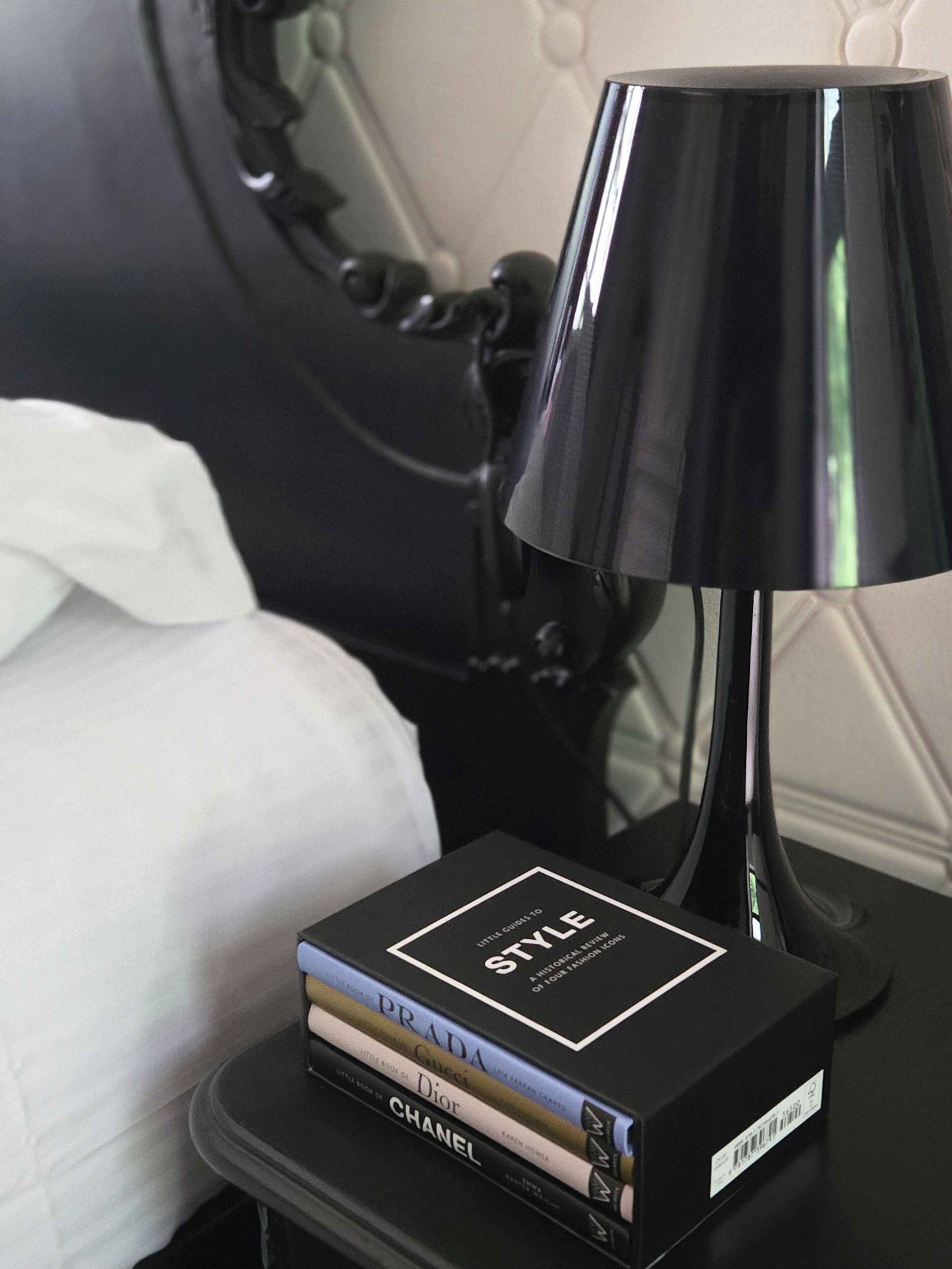 Een zwart nachtkastje met een zwarte lamp en een stapel boeken met de titel 'STYLE'.