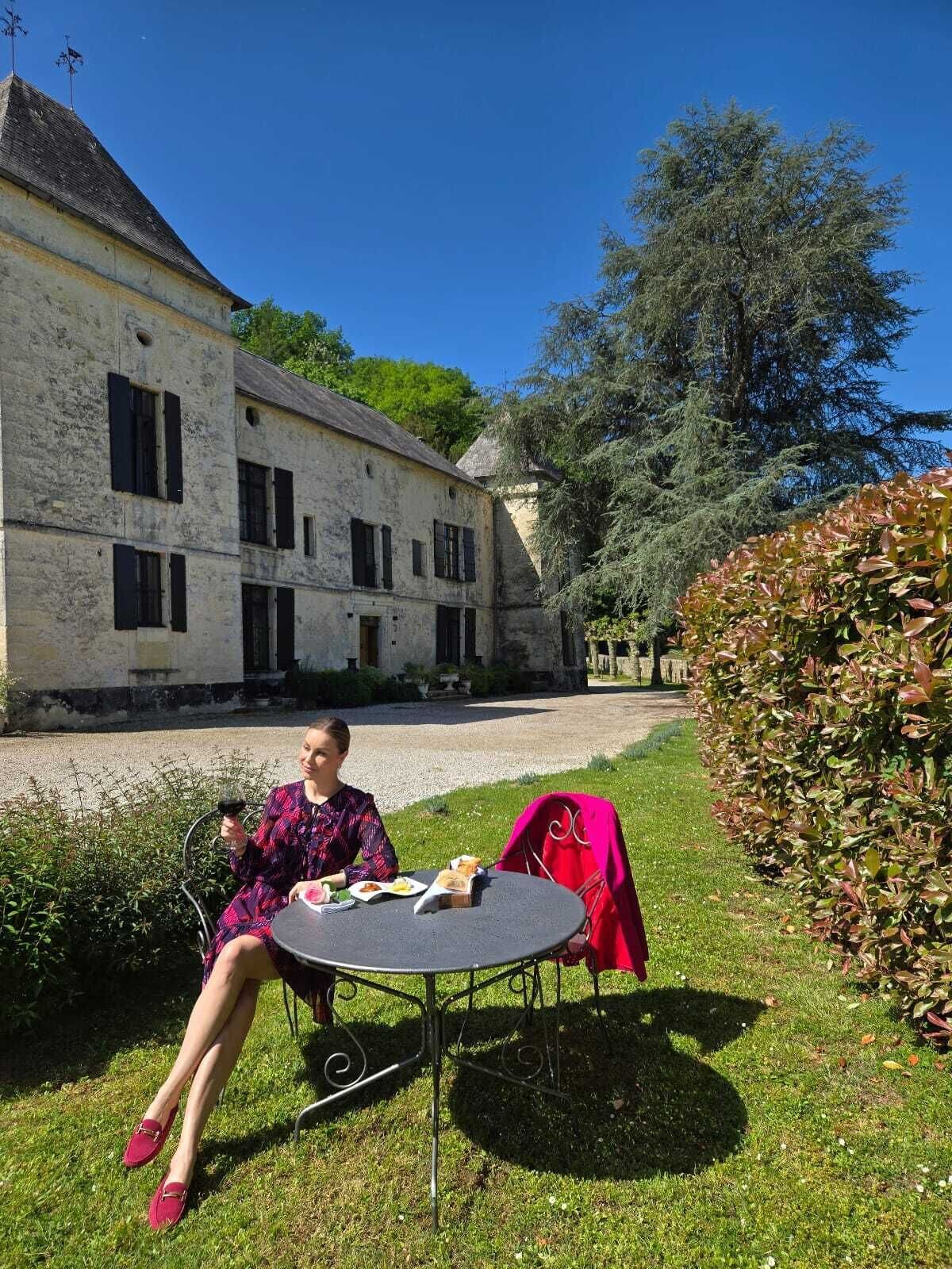A woman sitting at a round table outdoors with a building in the background.