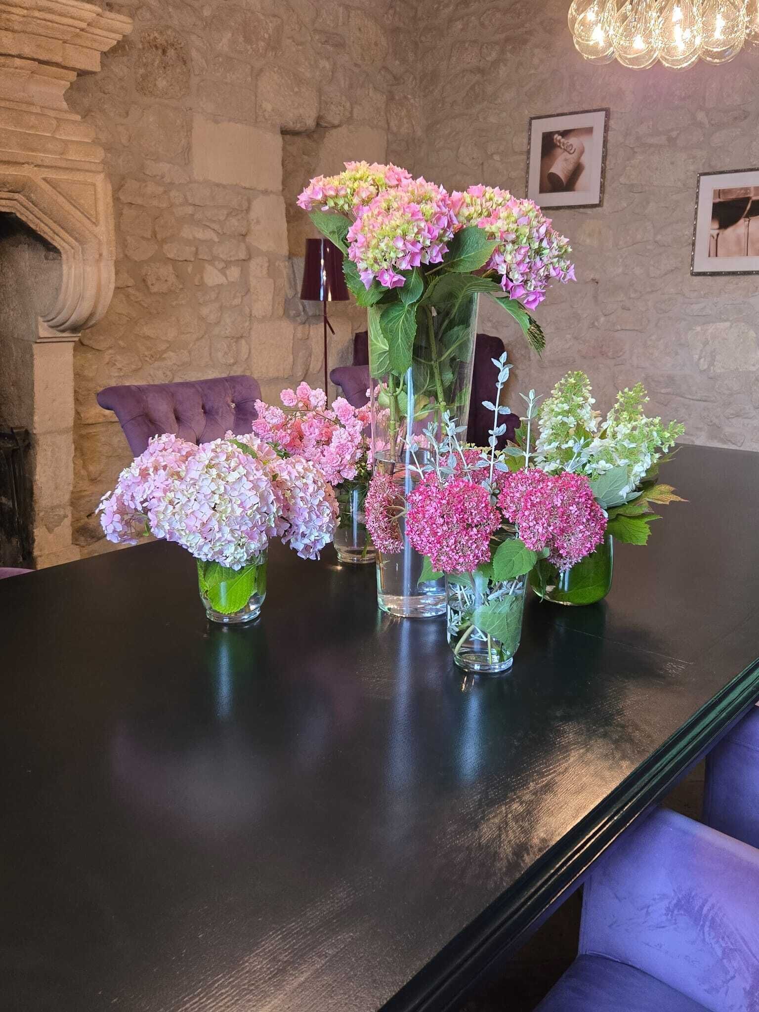 A dining table with multiple glass vases containing pink and white flowers.