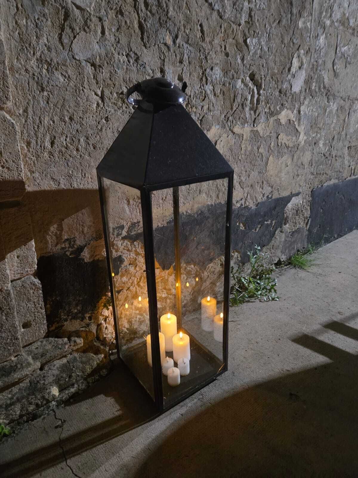 A lantern with multiple candles inside, placed on a stone surface against a textured wall.