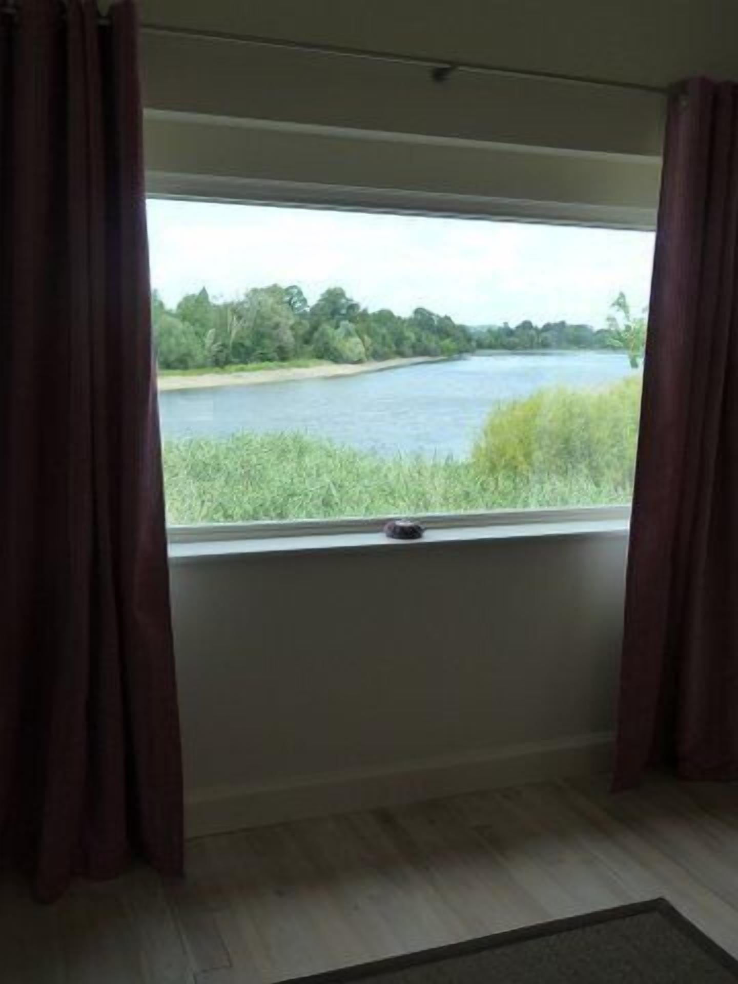 A room with a large window overlooking a river and greenery.