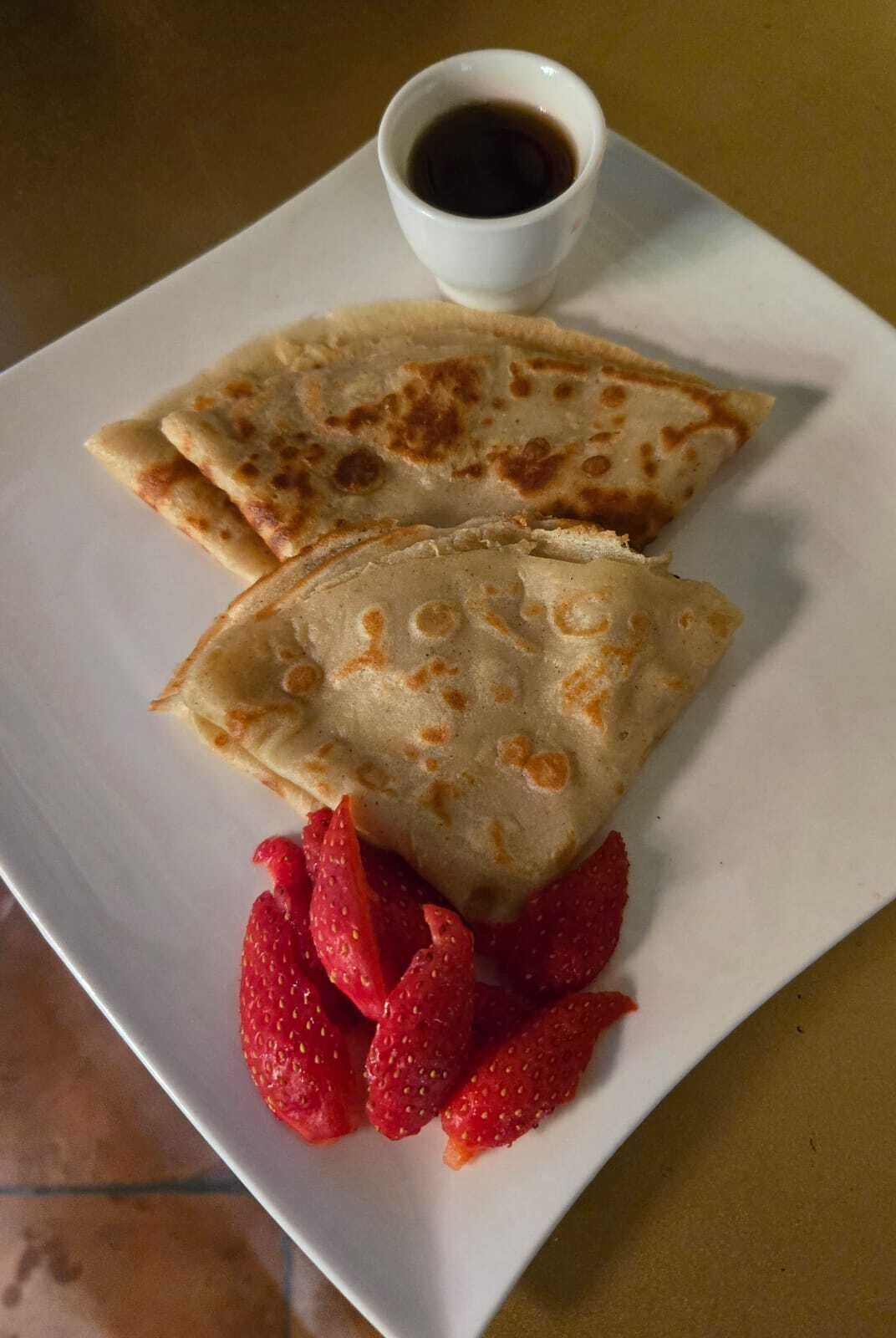 A plate with two crepes, strawberries, and a cup of coffee.