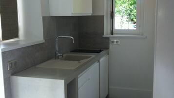 Cocina compacta con pileta, alacenas y ventana con vista a follaje.