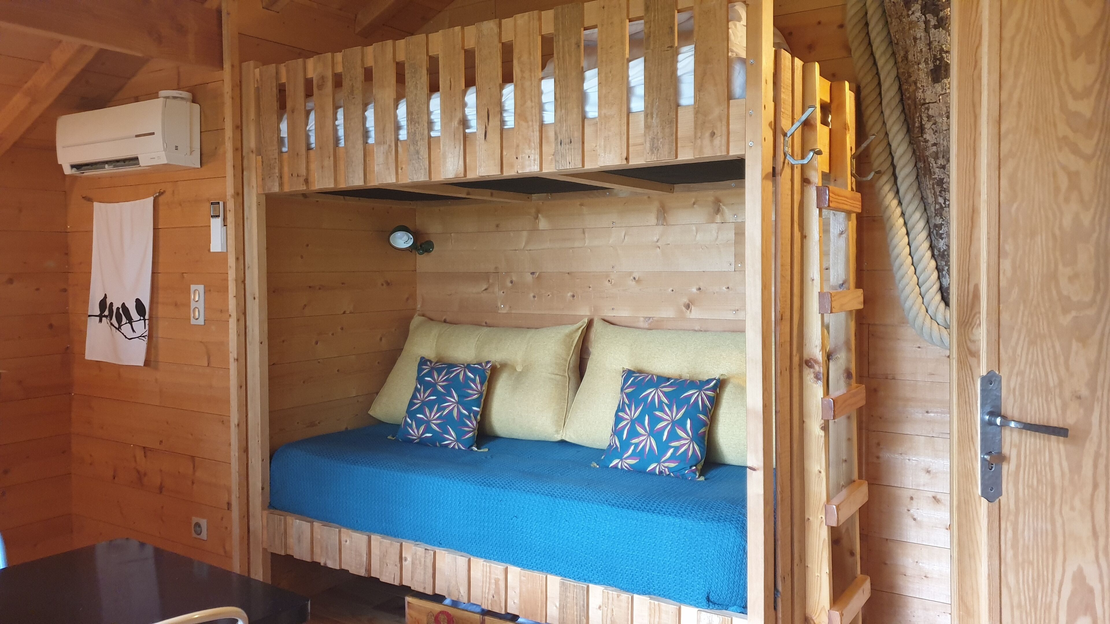 Une chambre dans un chalet en bois, avec un lit superposé, un climatiseur fixé au mur et une petite horloge.