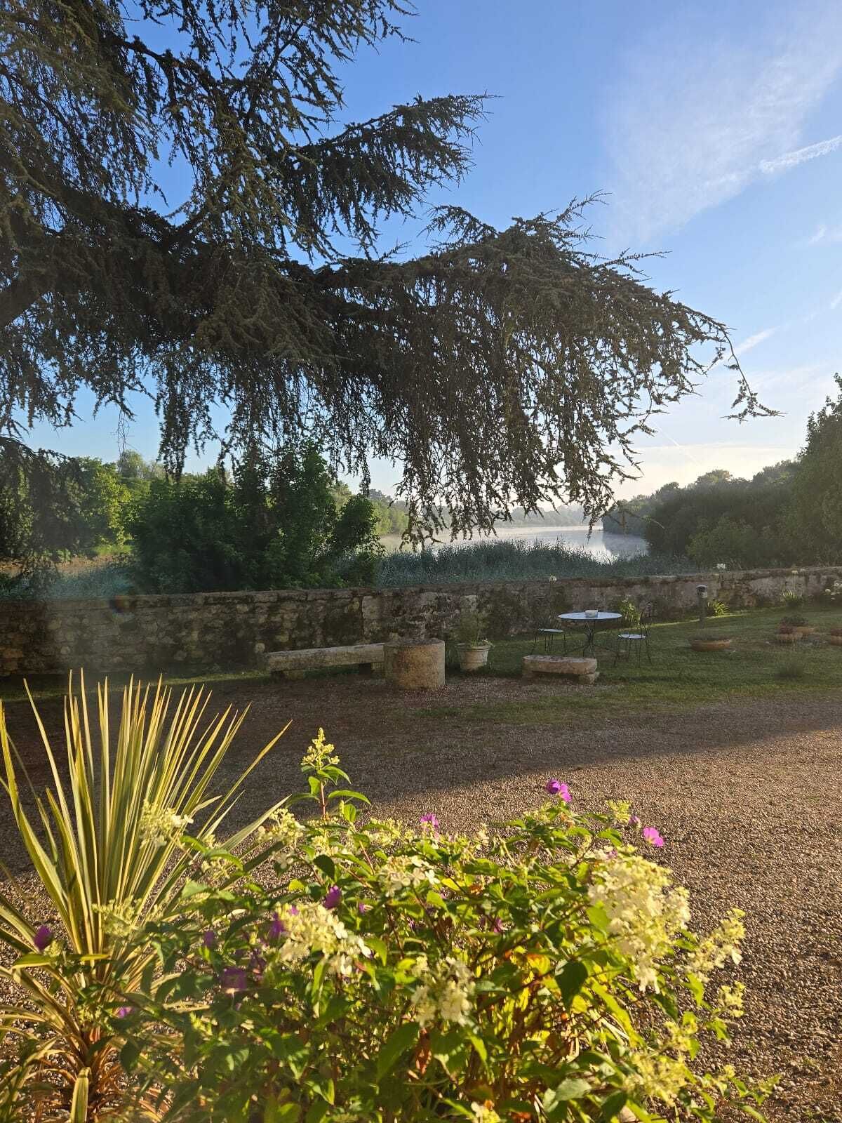 Un jardin avec un mur de pierres, un chemin de gravier et une table entourée de chaises.