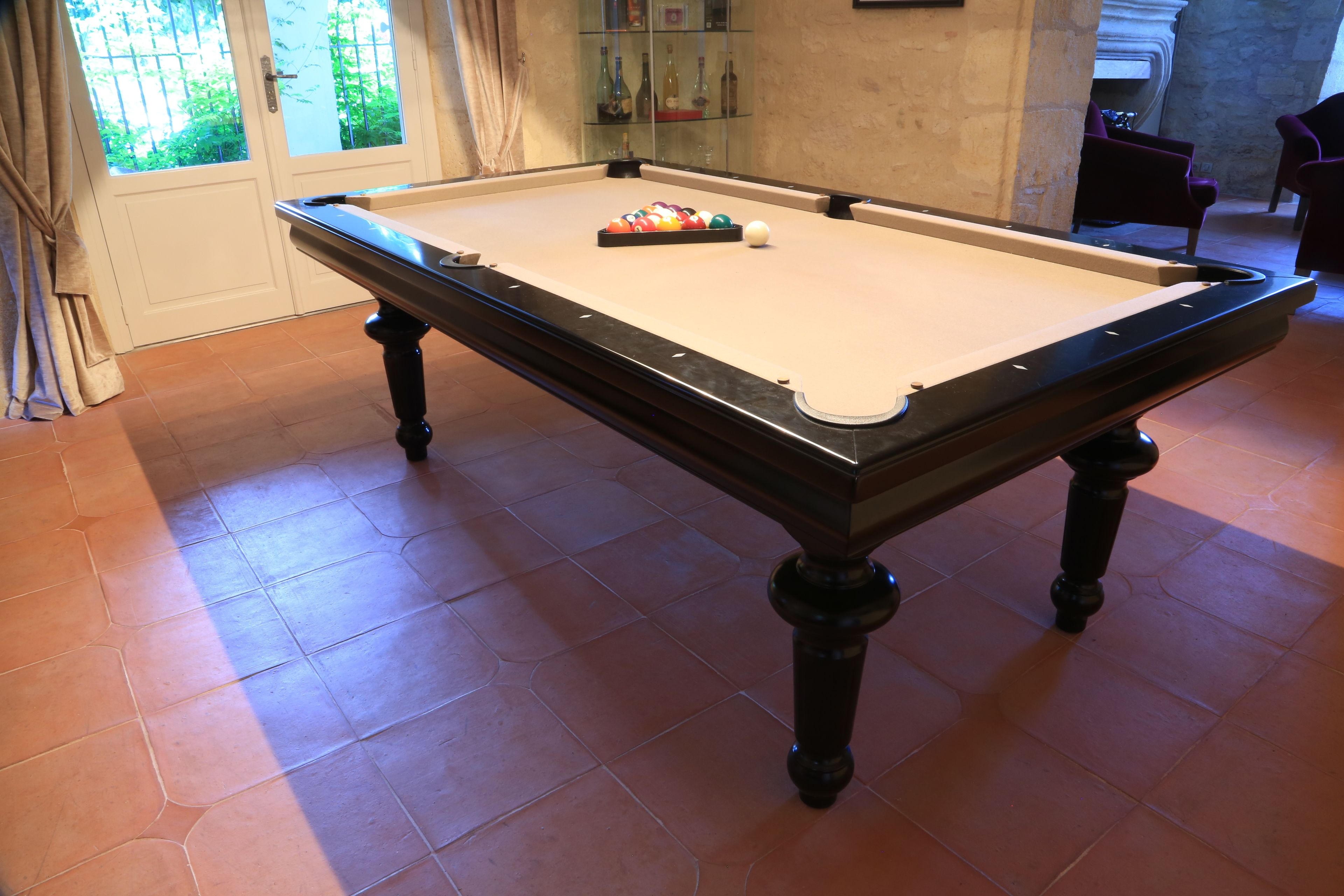 A pool table with balls, a glass cabinet with bottles, and a door with curtains.