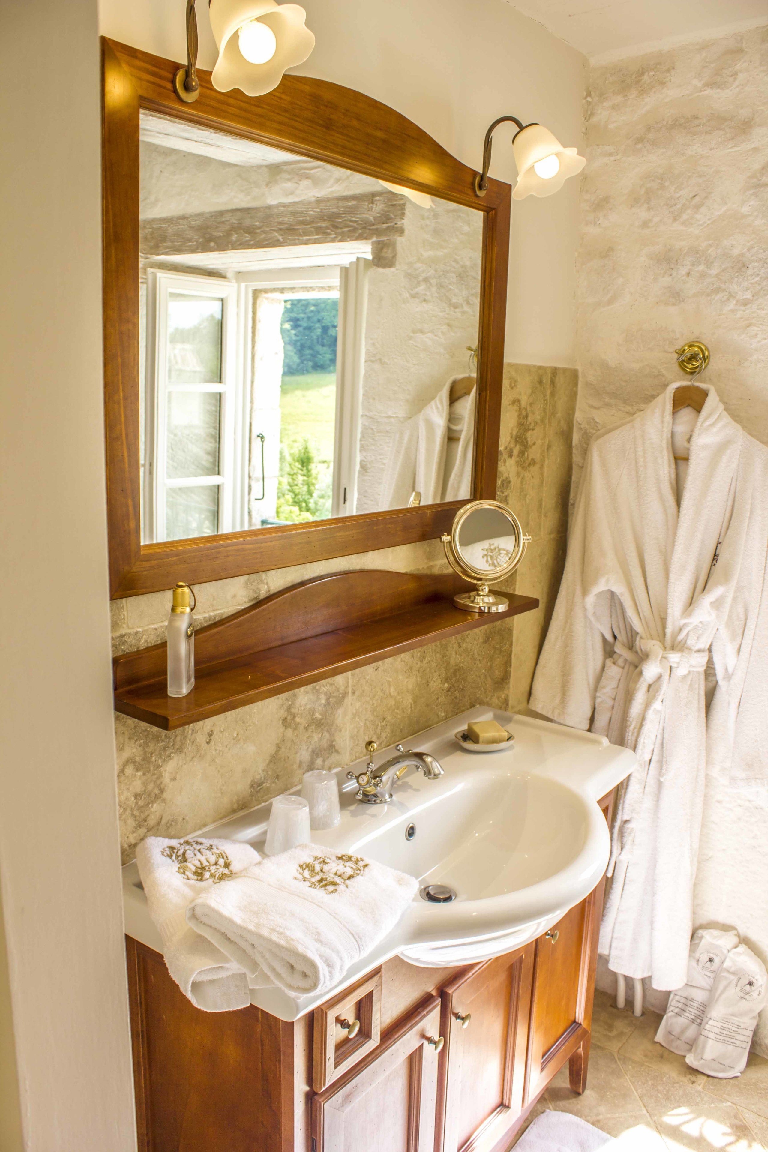 Une salle de bain avec un meuble-lavabo en bois, un grand miroir et un peignoir accroché au mur.