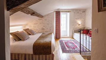 A bedroom with a sloped ceiling, a bed with patterned pillows, a red and white rug, and a small balcony with a railing.