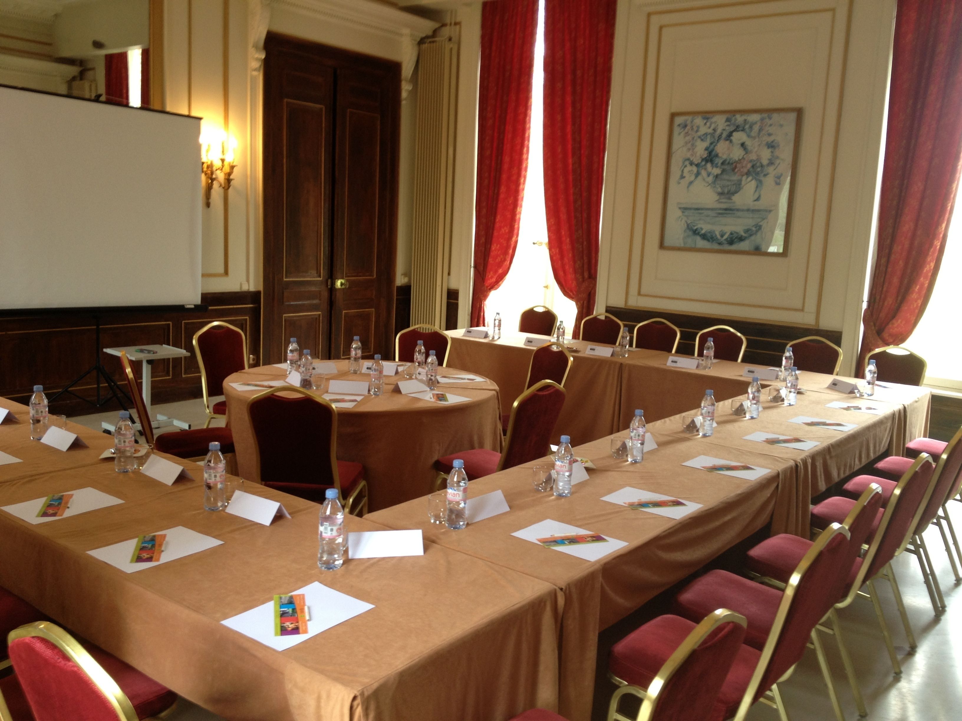 A conference room with long tables, red chairs, water bottles, and nameplates.