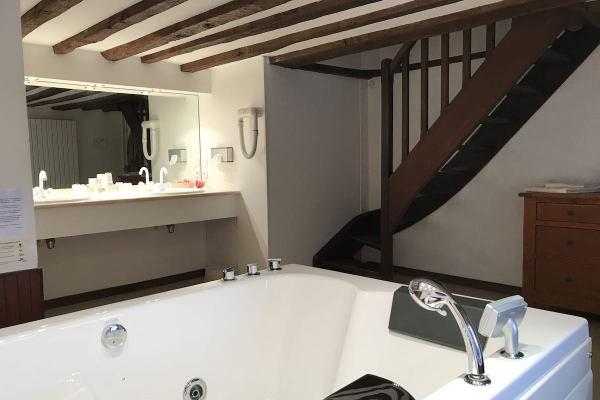 Un baño moderno con una bañera grande, una escalera de madera y un tocador con espejo.