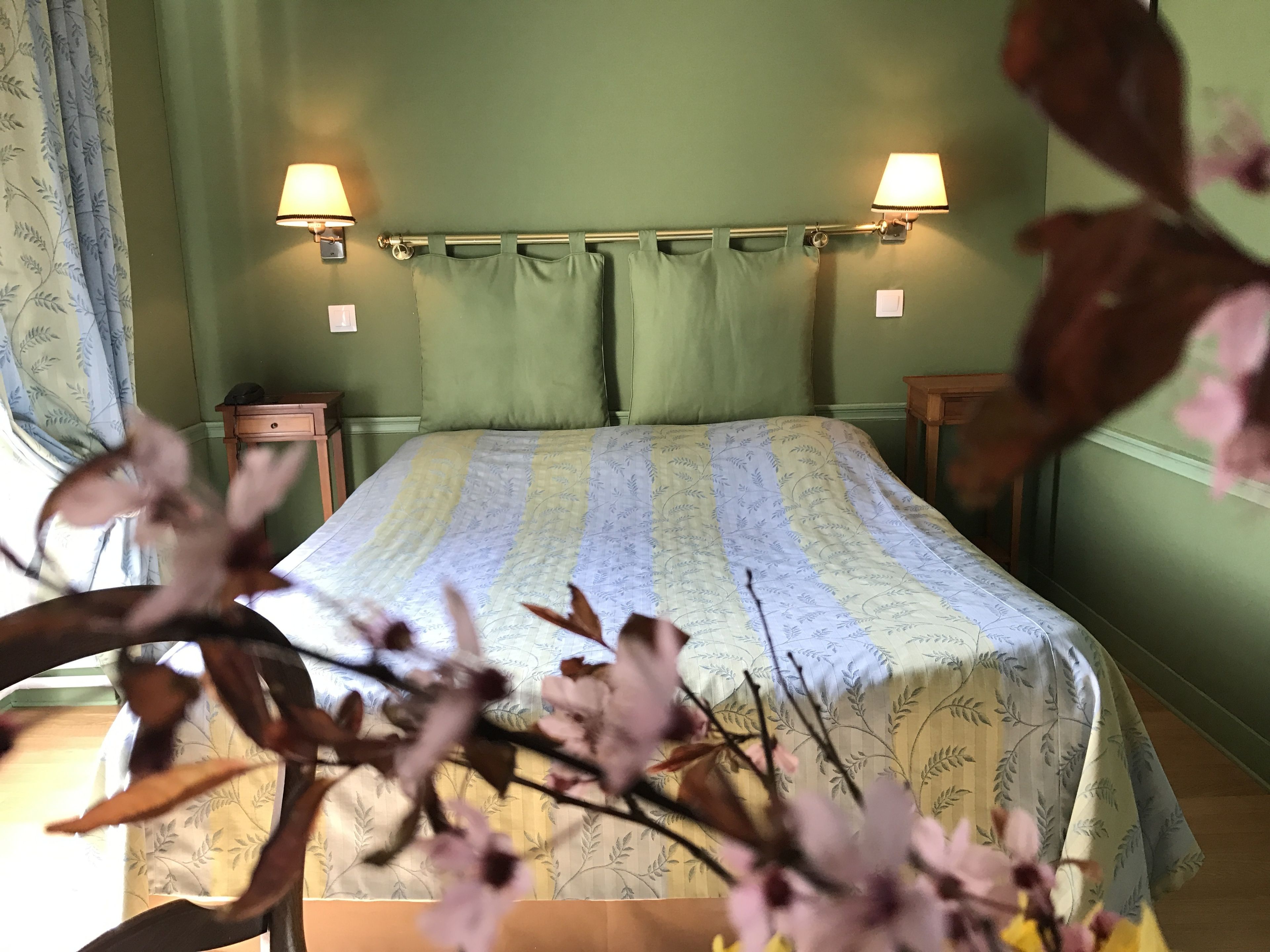 Un dormitorio con cama, dos lámparas de noche, una mesita de noche y una ventana con cortinas.