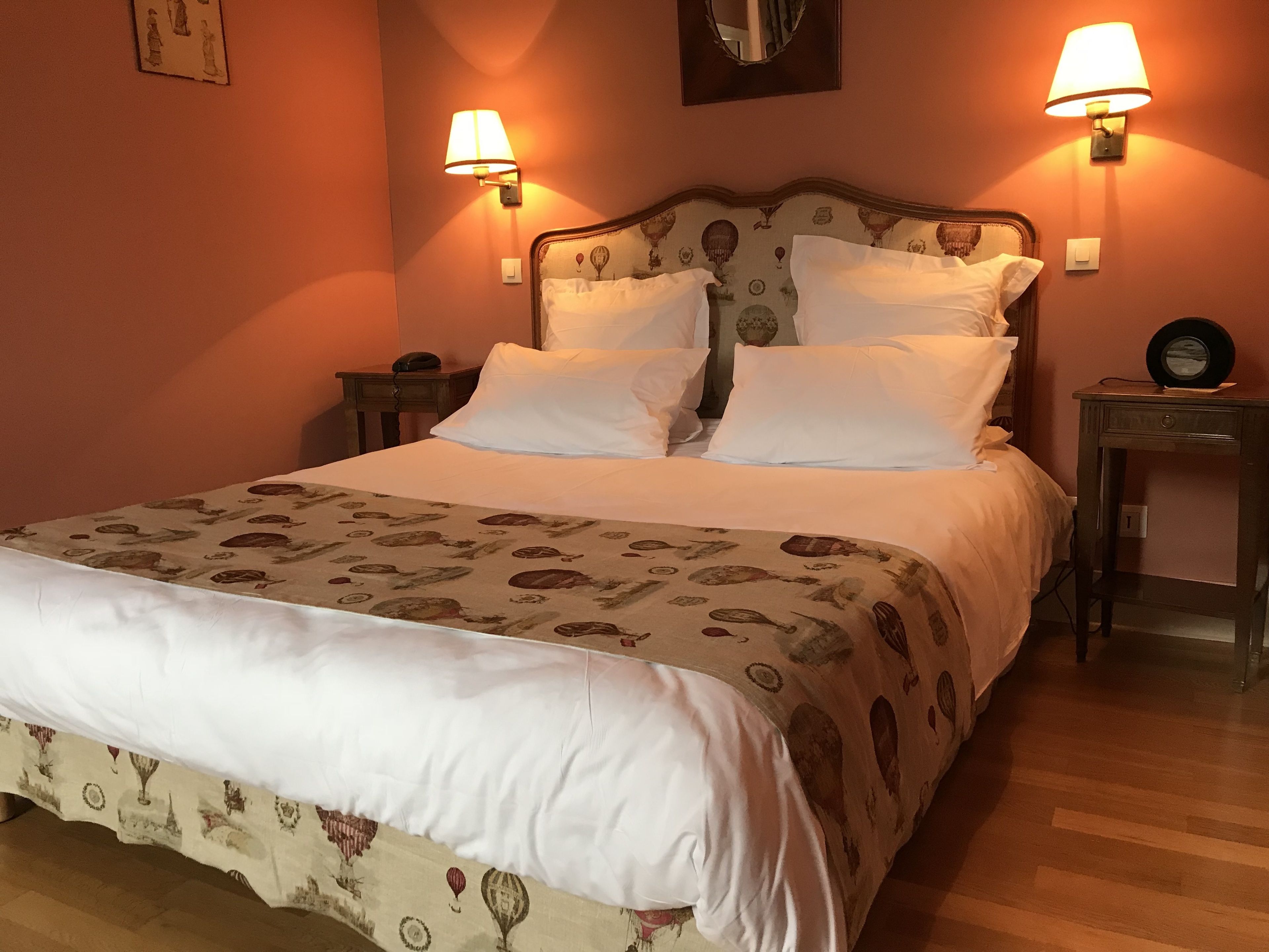 A neatly made bed with a patterned bedspread, two bedside lamps, and a small table with a clock.