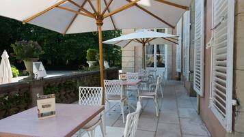 An outdoor patio area with white wicker furniture, large umbrellas, and a stone wall.