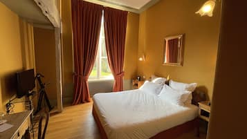 Ein Hotelzimmer mit einem großen Bett, einem Fernseher auf einem Schrank, einem Fenster mit roten Vorhängen und einem Spiegel an der Wand.