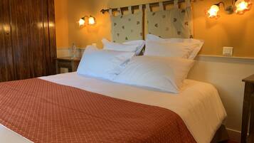 A hotel room with a large bed, white bedding, a wooden headboard, a nightstand with a bottle, and wall-mounted lights.