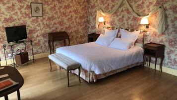 Un dormitorio con cama, mesitas de noche, un banco, un mueble para televisor y un papel tapiz floral.
