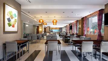 A modern restaurant with a long counter, multiple tables, and chairs. There is a large painting on the wall and a kitchen area in the background.