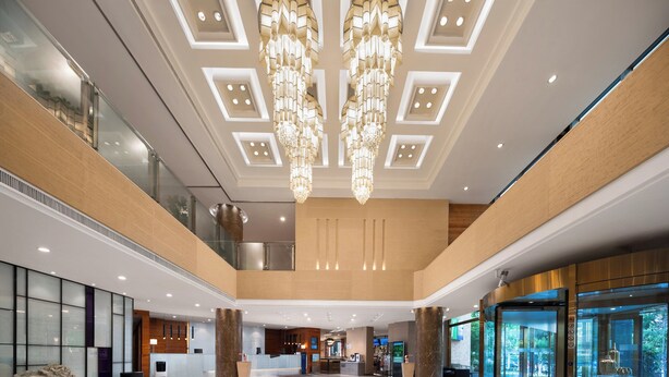 Een ruime lobby met een hoge plafond, moderne kroonluchters en een receptiebalie.