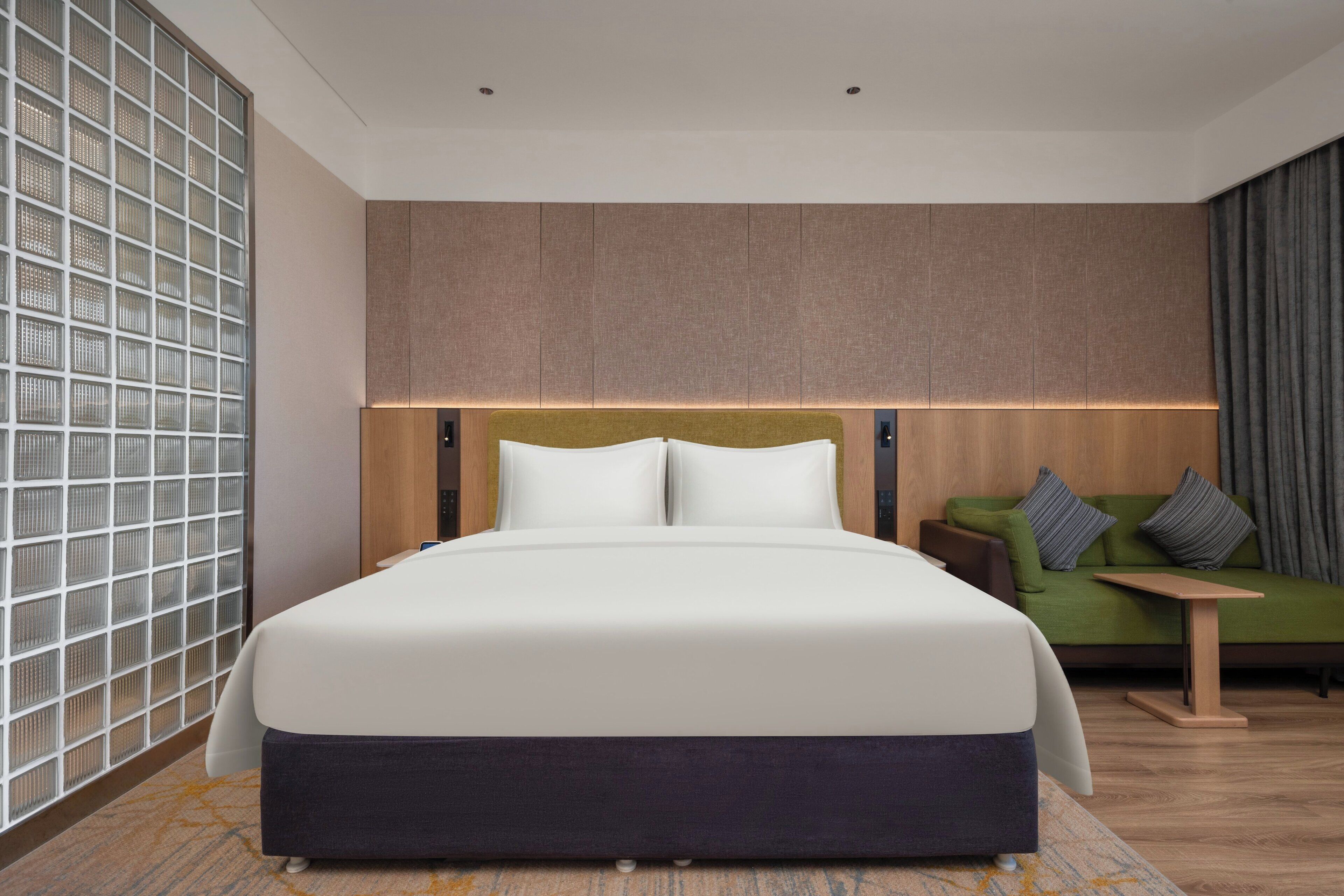 A modern hotel room with a large bed, a green sofa, and a small table.