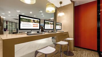 Un área de recepción con tres monitores de ordenador mostrando contenido promocional, un mostrador de recepción y dos taburetes de bar.