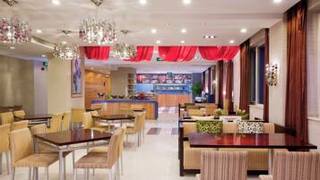 A hotel dining area with tables and chairs, a central bar, and decorative lighting.