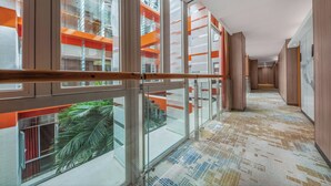 Een moderne hotelgang met glazen balustrades, een kamerbreed tapijt met dessin en uitzicht op een oranje gebouw.