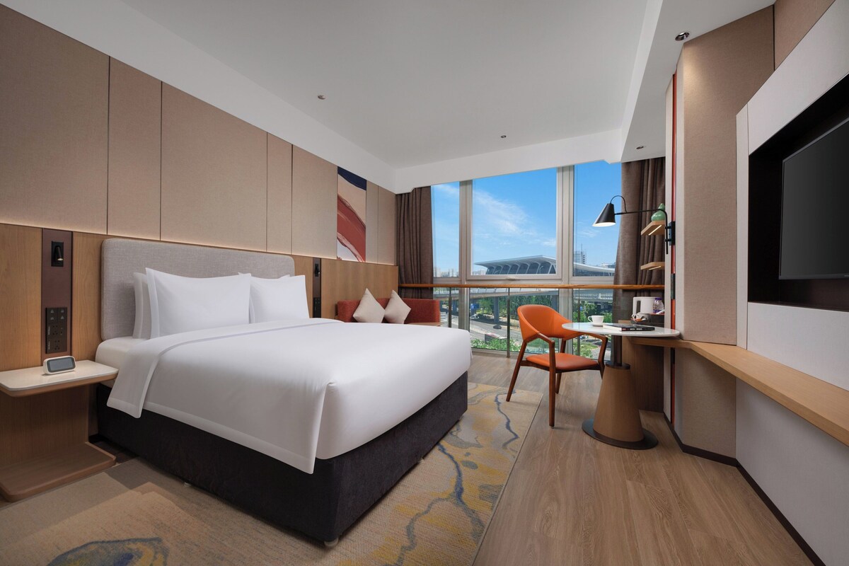 A modern hotel room with a large bed, a desk, and a TV.