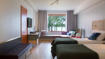 Une chambre d’hôtel équipée d’un lit, d’un bureau, d’une chaise, d’une télévision et d’une fenêtre donnant sur la verdure.