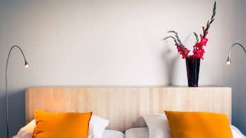 A hotel room with a wooden headboard, white bedding, and two orange pillows.