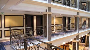 Hotelinterieur met meerdere verdiepingen, een centrale trap, diverse balkons en een lobby met zitplaatsen.