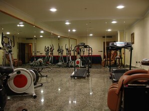 Un gimnasio con diferentes máquinas de ejercicio, un espejo grande en la pared y suelo cubierto de alfombra.