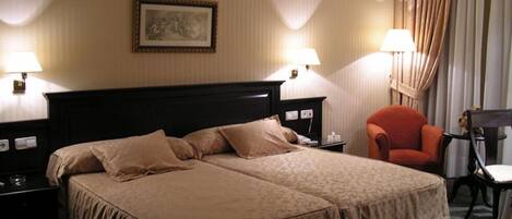 Una habitación de hotel con una cama doble, dos mesitas de noche, una silla y un escritorio con lámpara.