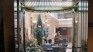 Een glazen liftinrichting met een rond vloerplan, een centraal decoratief element en een zithoek met stoelen en een tafel.