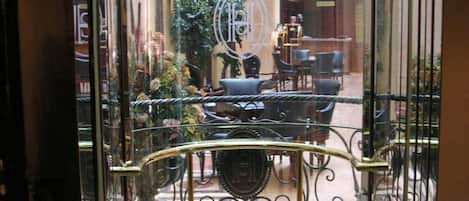 A glass elevator entrance with a circular floor plan, a central decorative element, and a seating area with chairs and a table.