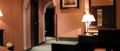 Quarto de hotel com cama, escrivaninha, cadeira, abajur e quadro na parede.