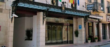 Fachada de hotel de estilo arquitectónico clásico, con una entrada destacada que incluye puertas de vidrio y un toldo de metal.