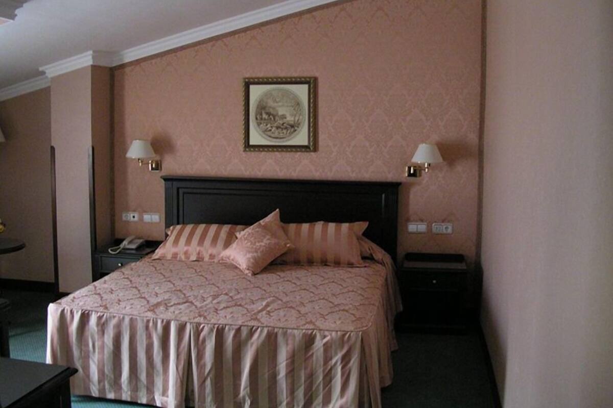 A hotel room with a large bed, two bedside lamps, a nightstand, and a framed picture on the wall.
