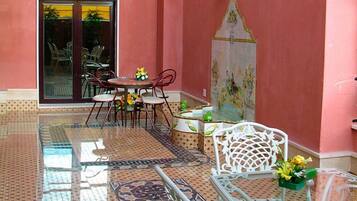 Un comedor con una mesa y sillas de vidrio, piso de baldosas y pared decorada con un mural de azulejos.