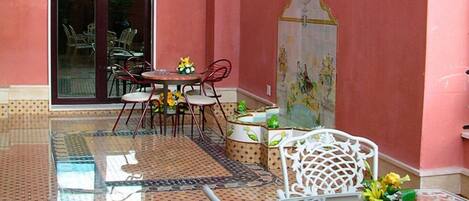 A dining area with a glass table and chairs, a tiled floor, and a decorative wall with a tiled mural.