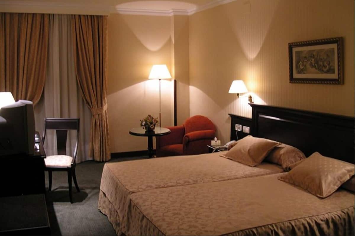A hotel room with two beds, a desk, a chair, and two lamps.