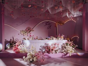 Ein Empfangsbereich mit einer weißen Rezeption, Blumenarrangements und einer dekorativen Decke mit hängenden Elementen.