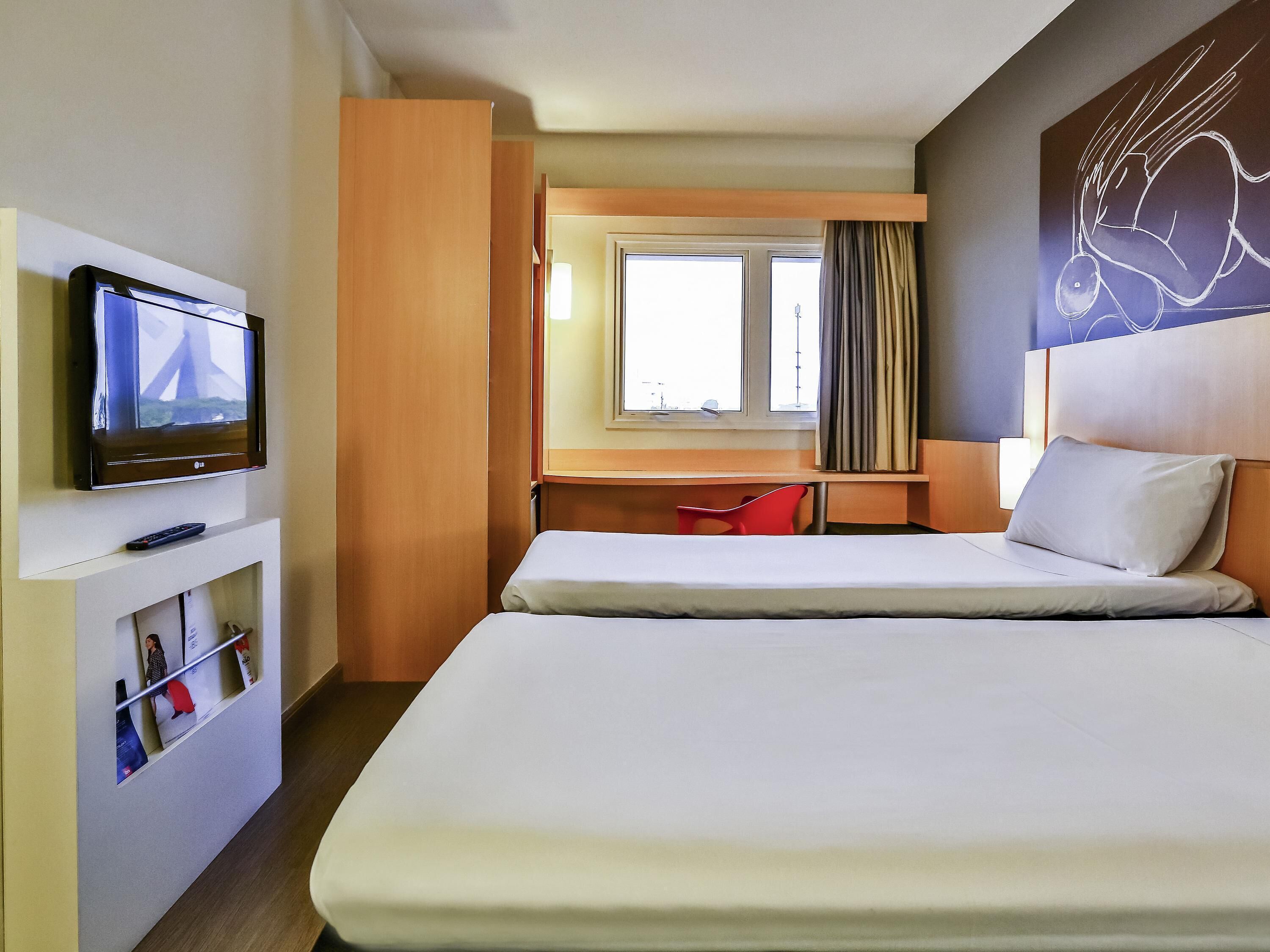 Una habitación de hotel con cama, escritorio con silla, televisor y ventana con cortinas.