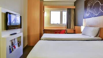 Una habitación de hotel con cama, escritorio con silla, televisor y ventana con cortinas.