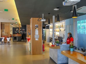A modern interior with a reception desk, seating area, and a bar. - Ibis Goiania (Goiania)