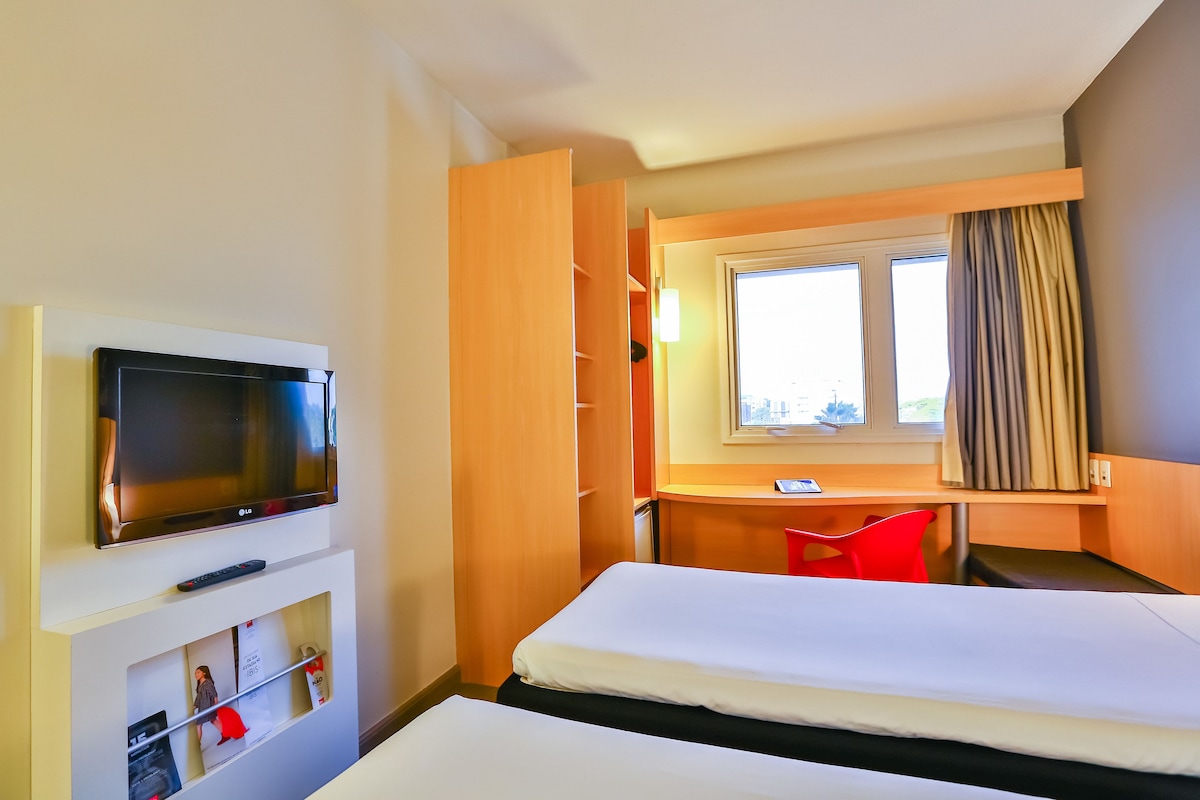 A hotel room with a bed, a desk, a TV, and a wardrobe.